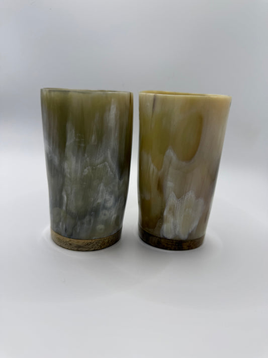 Two small natural horn cups with pale cream gray and honey tones on a white background