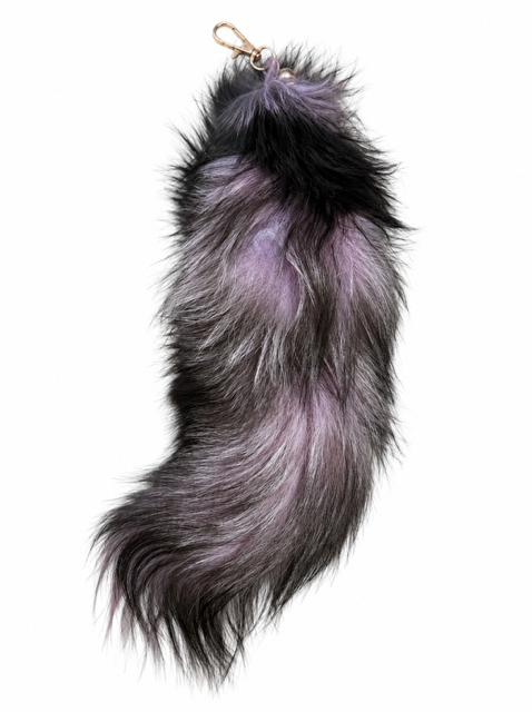 A fox fur keychain or bag charm with a gold-tone lobster clasp, featuring a shaggy texture in black, gray, and lavender-purple tones, isolated on a white background.